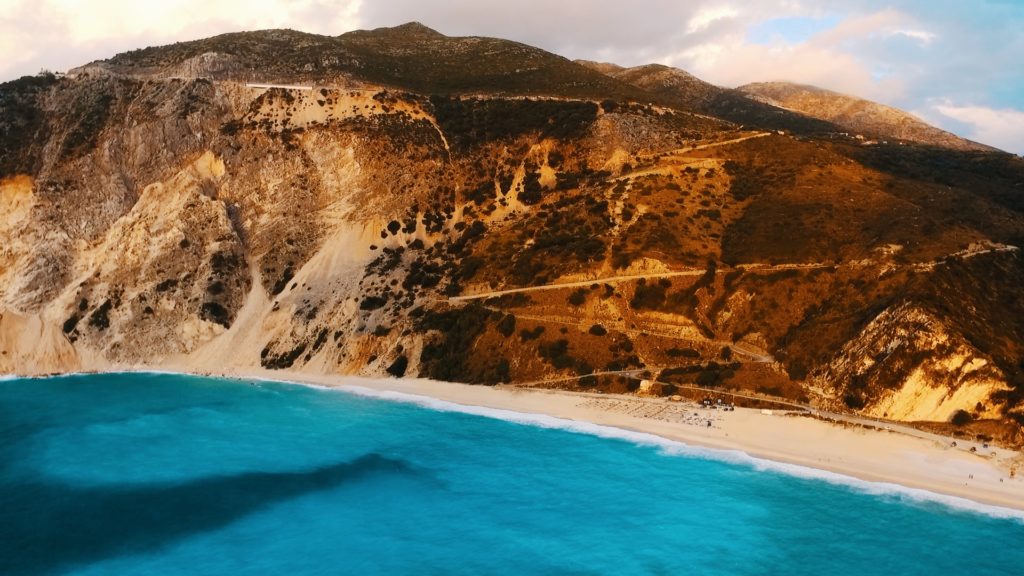 drone picture of mountains and driving route down to myrtos beach